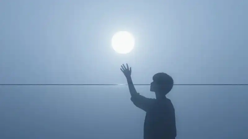 A silhouette reaches toward a glowing circle through glass